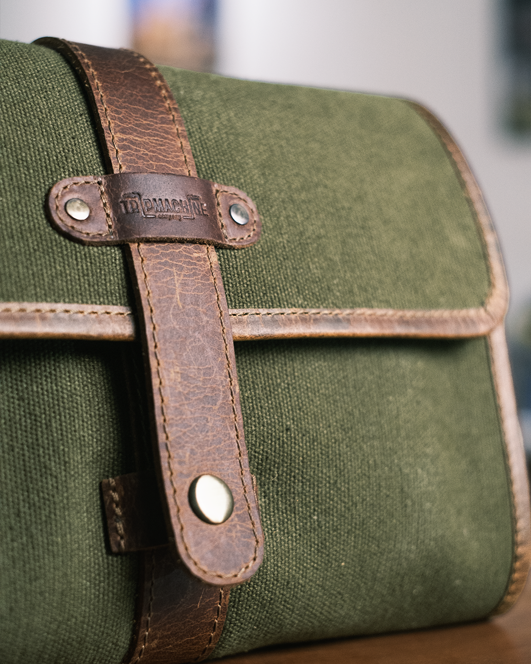Green canvas leather care kit with brown leather straps and hardware on a blurred background